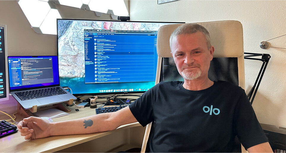 Jason Dunnivant sitting at his desk with his forearm out to show his Octopus Deploy tattoo